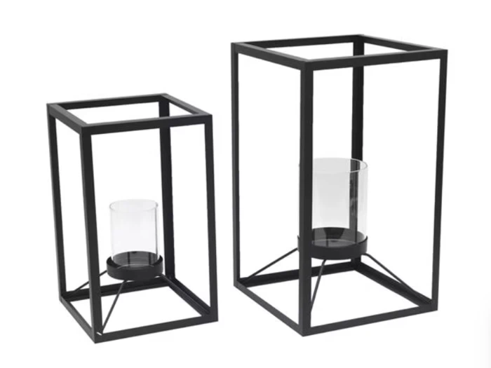 To rektangulære lanterner i sort metal i forskellige størrelser med hver sin lysestage i klart glas inde i den åbne ramme.
