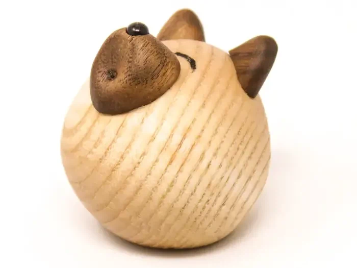 En rund træfigur, der ligner et kattehoved, med brune ører og næse og minimale ansigtstræk på en lys træstruktureret overflade.