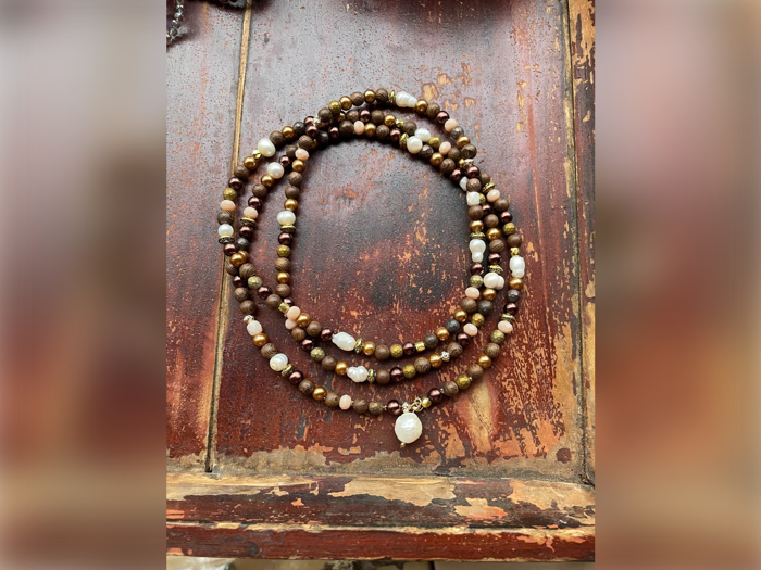 En perlekæde med brune, gyldne og hvide perler er rullet op på en forvitret træoverflade.