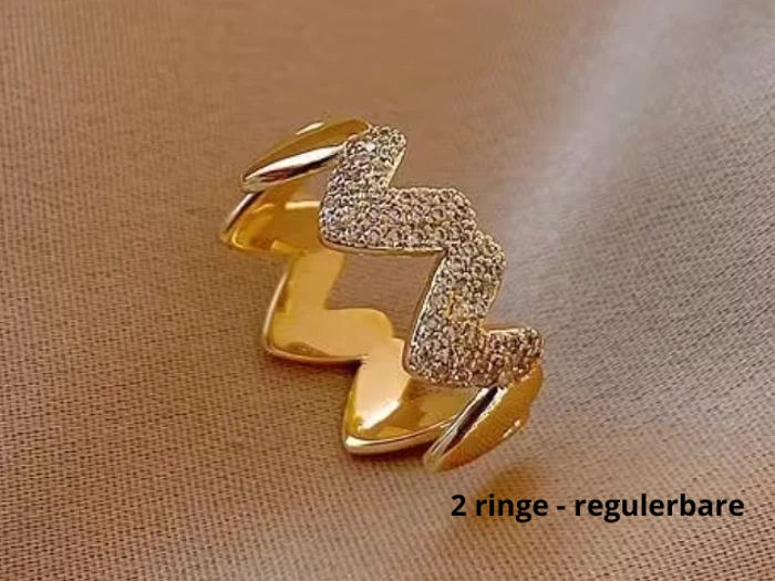 En justerbar guldring med zigzag-design, halvt glat og halvt besat med små krystaller, vist på beige stof. Tekst: 2 ringe - regulerbare.