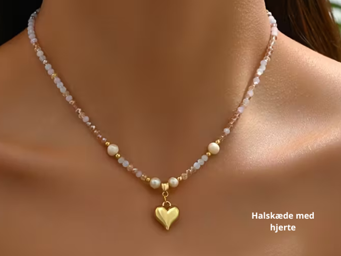 En delikat perlekæde med perler og et hjertevedhæng i guld, båret om en kvindes hals. Den danske tekst lyder: Halskæde med hjerte.