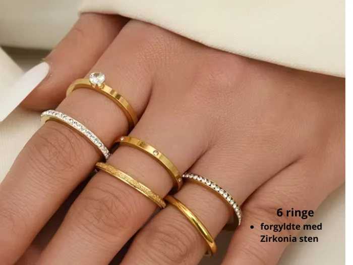 En hånd med seks guldringe med zirkonia-sten, vist ved siden af tekst på dansk: 6 ringe, forgyldte med Zirkonia sten.