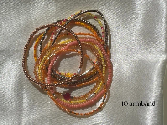 Et bundt med ti farverige perlearmbånd vises på et skinnende, lyst stof med teksten 10 armbånd i nederste højre hjørne.