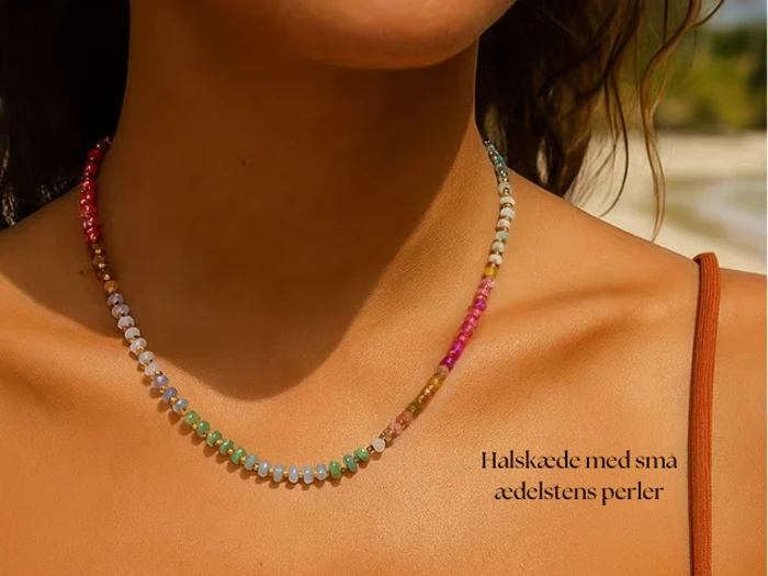 En kvinde bærer en fin halskæde med små, farverige ædelstensperler. Teksten på dansk lyder: Halskæde med små ædelstens perler.