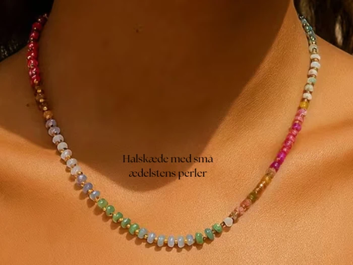 En kvinde bærer en delikat halskæde lavet af små, flerfarvede ædelstensperler. Teksten på billedet lyder: Halskæde med små ædelstens perler.