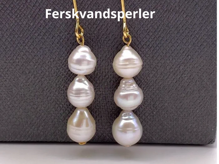 To guldøreringe med uregelmæssige hvide ferskvandsperler på en struktureret mørkegrå baggrund. Ordet Ferskvandsperler står øverst.