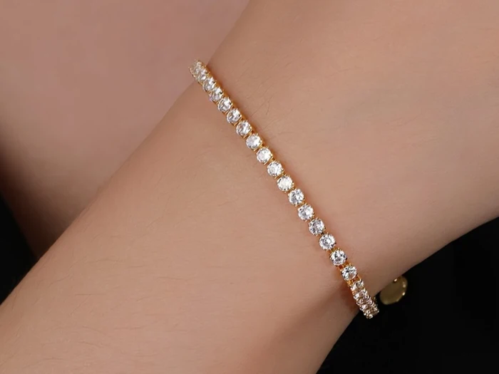 Et delikat tennisarmbånd med runde, funklende diamanter indfattet i et tyndt guldbånd, som bæres på en persons håndled.