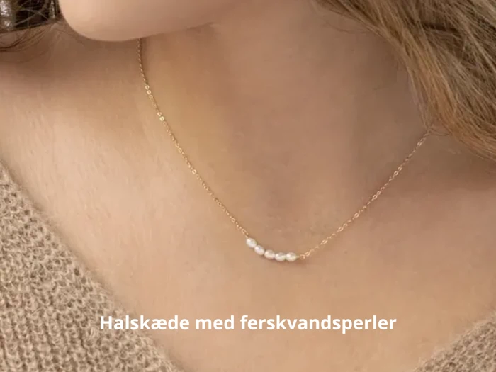 Nærbillede af en kvinde iført en delikat guldkæde med små ferskvandsperler. Teksten på dansk lyder: Halskæde med ferskvandsperler.