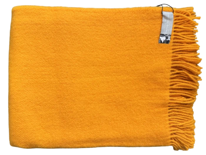 Et foldet lysegult uldtæppe med frynsede kanter og et mærke i øverste højre hjørne.