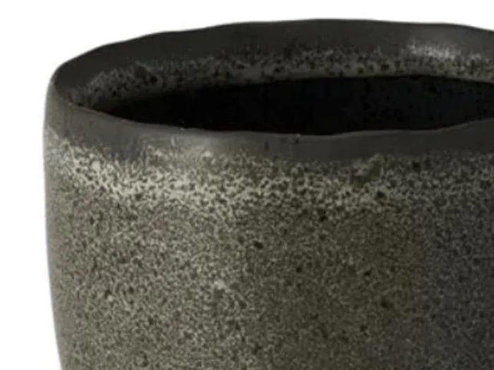 Nærbillede af en struktureret, mørkegrå keramikkop med en ujævn, let bølget kant mod en hvid baggrund.
