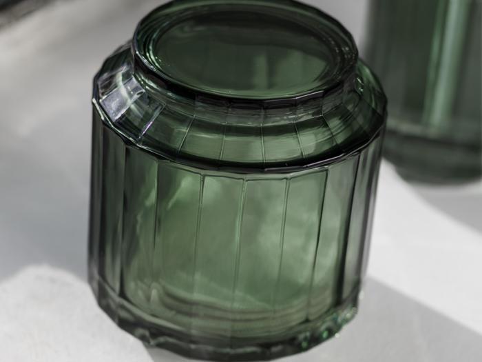 Nærbillede af en tom, mørkegrøn glaskrukke, der ligger på hovedet på en hvid flade og viser dens strukturerede, lodrette riller og flade bund.
