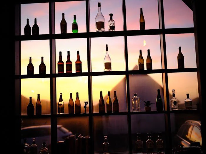 Flaskerne er anbragt på vindueshylder med en solnedgangshimmel og bygningssilhuetter synlige udenfor.