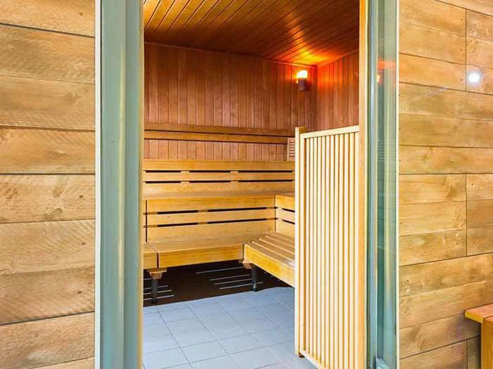 En åben dør afslører en moderne træsauna med bænke, panelvægge og et varmt lys monteret på væggen indeni.