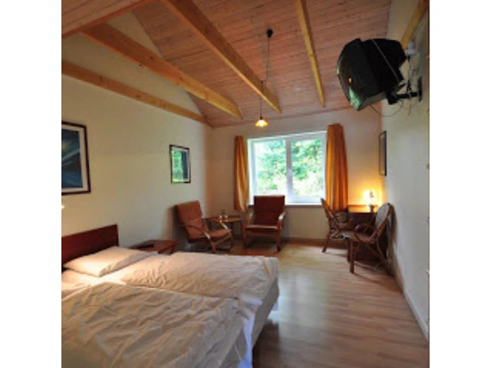 Et hyggeligt soveværelse med dobbeltseng, træbjælker i loftet, stole ved et vindue med gule gardiner, et lille bord og et væghængt tv.