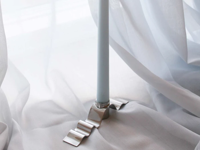 En hvid stang står på en glat, skinnende sølvbase oven på et blødt, hvidt stof med gennemsigtige gardiner, der er samlet løst omkring den.