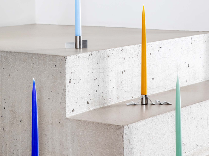 Fire farverige stearinlys - blå, lyseblå, gul og lysegrøn - står i moderne metalholdere på betontrin med en minimal, moderne baggrund.