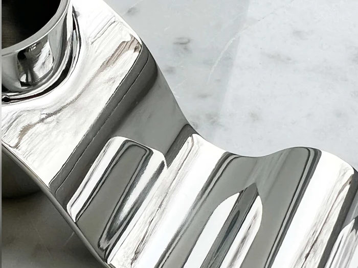 Nærbillede af en skinnende, buet metalgenstand med riller, der hviler på en lys, marmorlignende overflade.