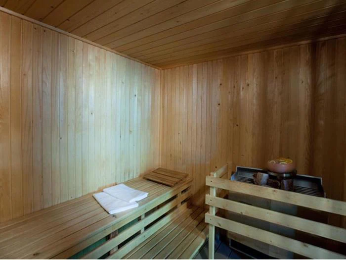 Et saunarum i træ med en bænk, to foldede hvide håndklæder og en ovn med sten i hjørnet.