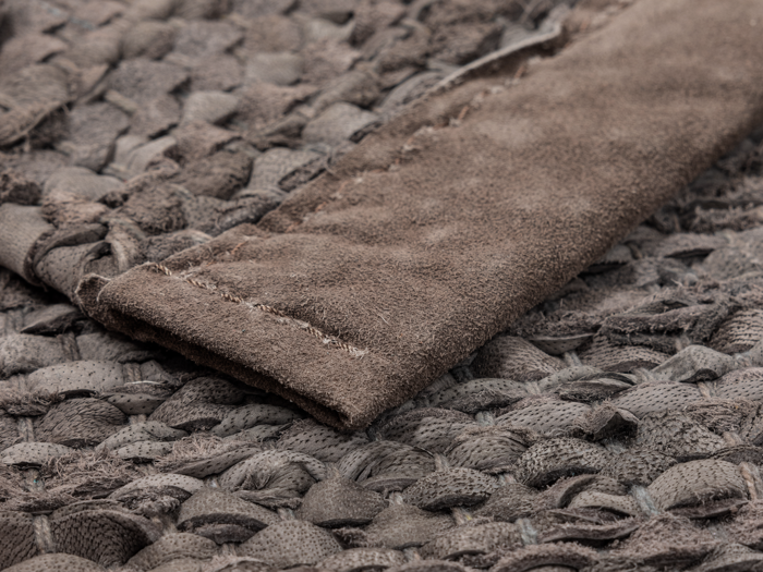 Nærbillede af et vævet, struktureret stof i brune nuancer med en foldet ruskindslignende strimmel ovenpå.