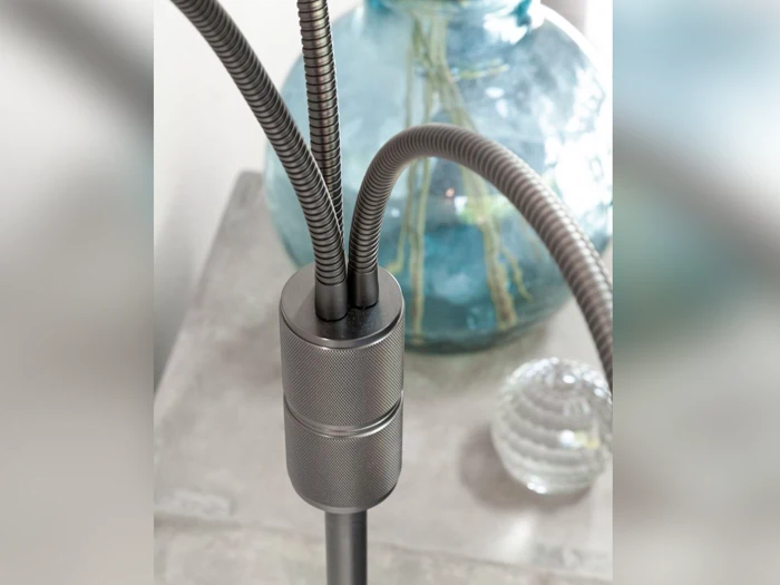 Nærbillede af en metallisk, fleksibel svanehalslampe med tre arme foran en stor blå glasvase og en lille klar, struktureret glaskugle.