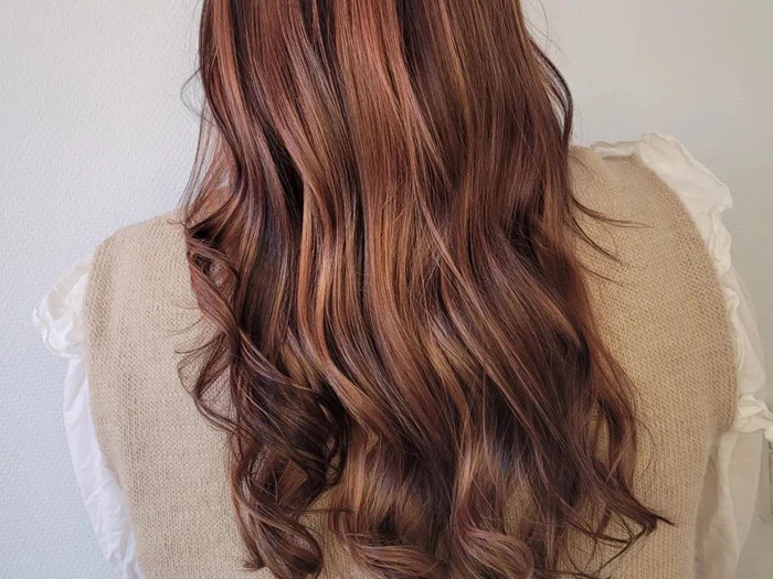 En person med langt, bølget, rødbrunt hår ses bagfra iført en beige vest over en hvid top.