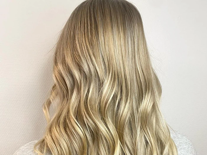 En person med langt, bølget, blondt hår vises bagfra mod en almindelig, lys baggrund.