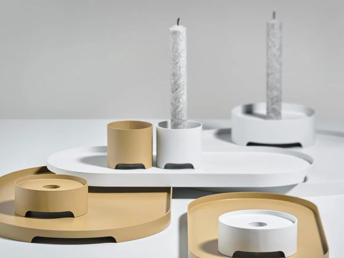 Minimalistiske lysestager og bakker i beige og hvide toner med moderne, geometriske former, udstillet på en flad overflade. Et lys er delvist brændt.