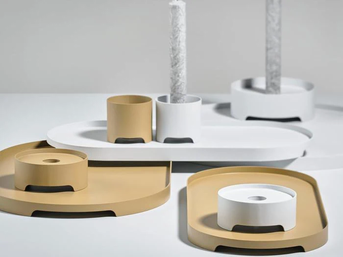 Minimalistiske guld- og hvide bakker og cylindriske holdere, hvoraf nogle bærer teksturerede hvide lys, arrangeret på en lys overflade.