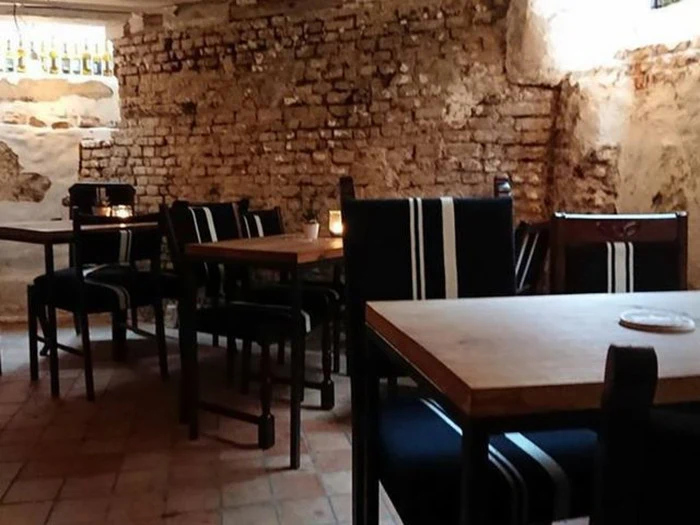 En hyggelig café med murstensvægge, træborde og sorte stole med hvide striber. Tændte stearinlys står på bordene og skaber en varm atmosfære.