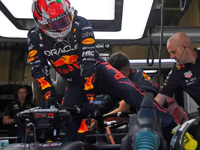 En Formel 1-kører i Red Bull-dragt stiger ind i en bil i garagen, hjulpet af teammedlemmer i sorte uniformer.